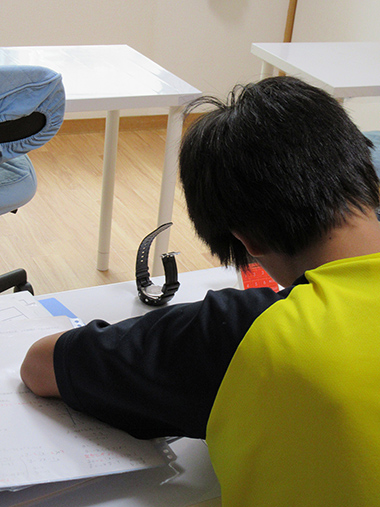 教材を積み上げて宿題に集中する男子生徒の後ろ姿。